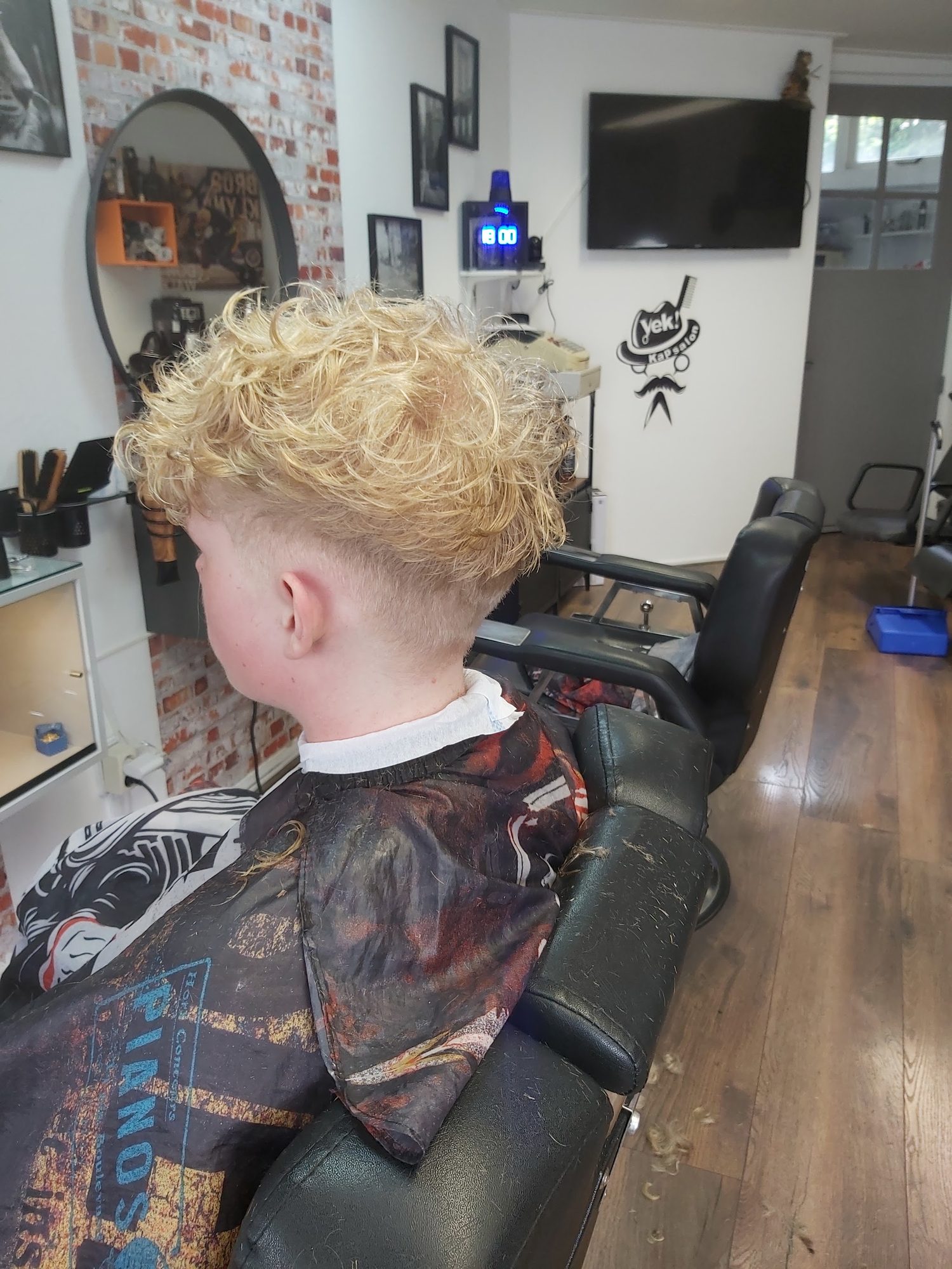 Jonge klant van achteren met krullend blond haar bovenop en een korte fade