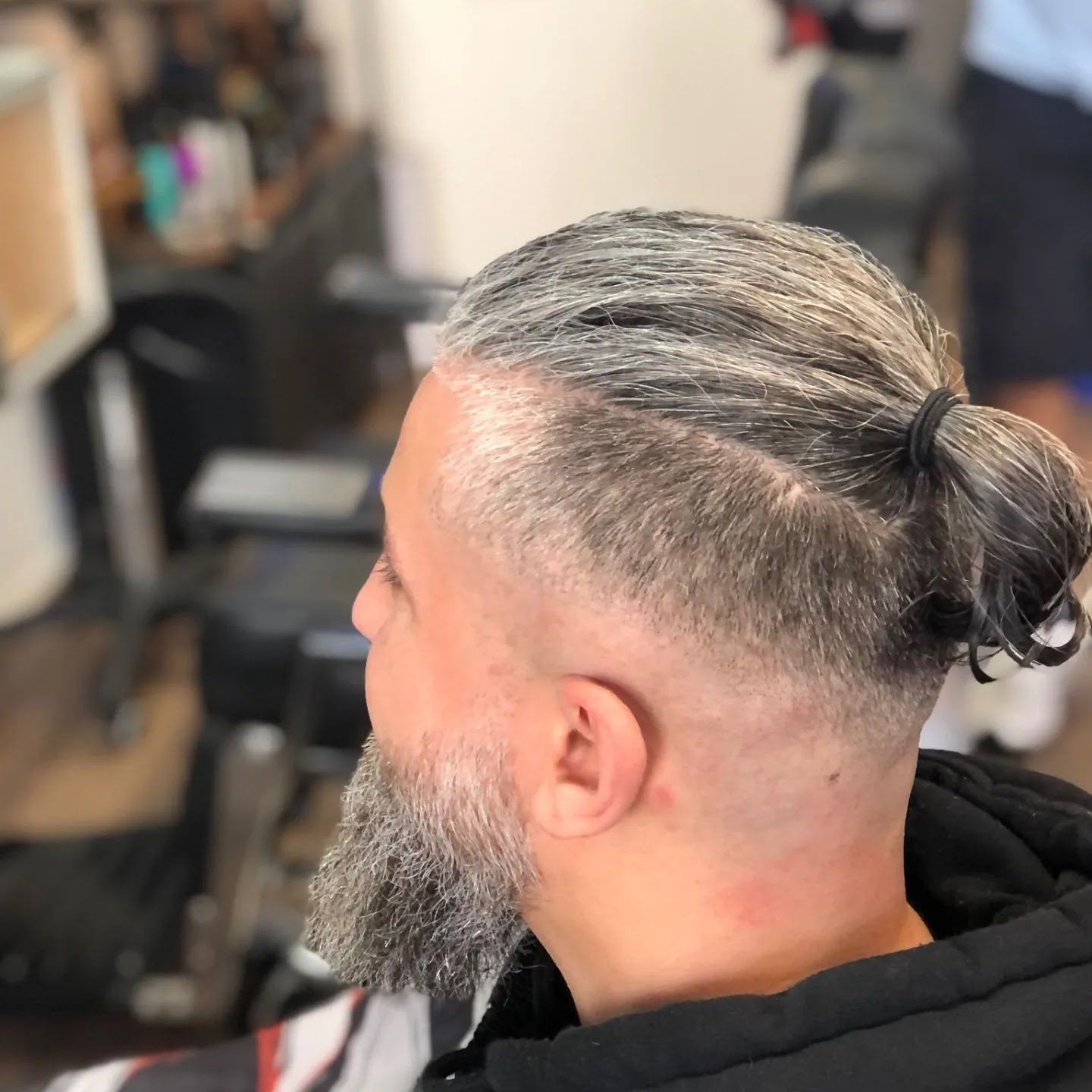 Man met grijs haar in een knot, korte zijkanten en grijze baard, van opzij